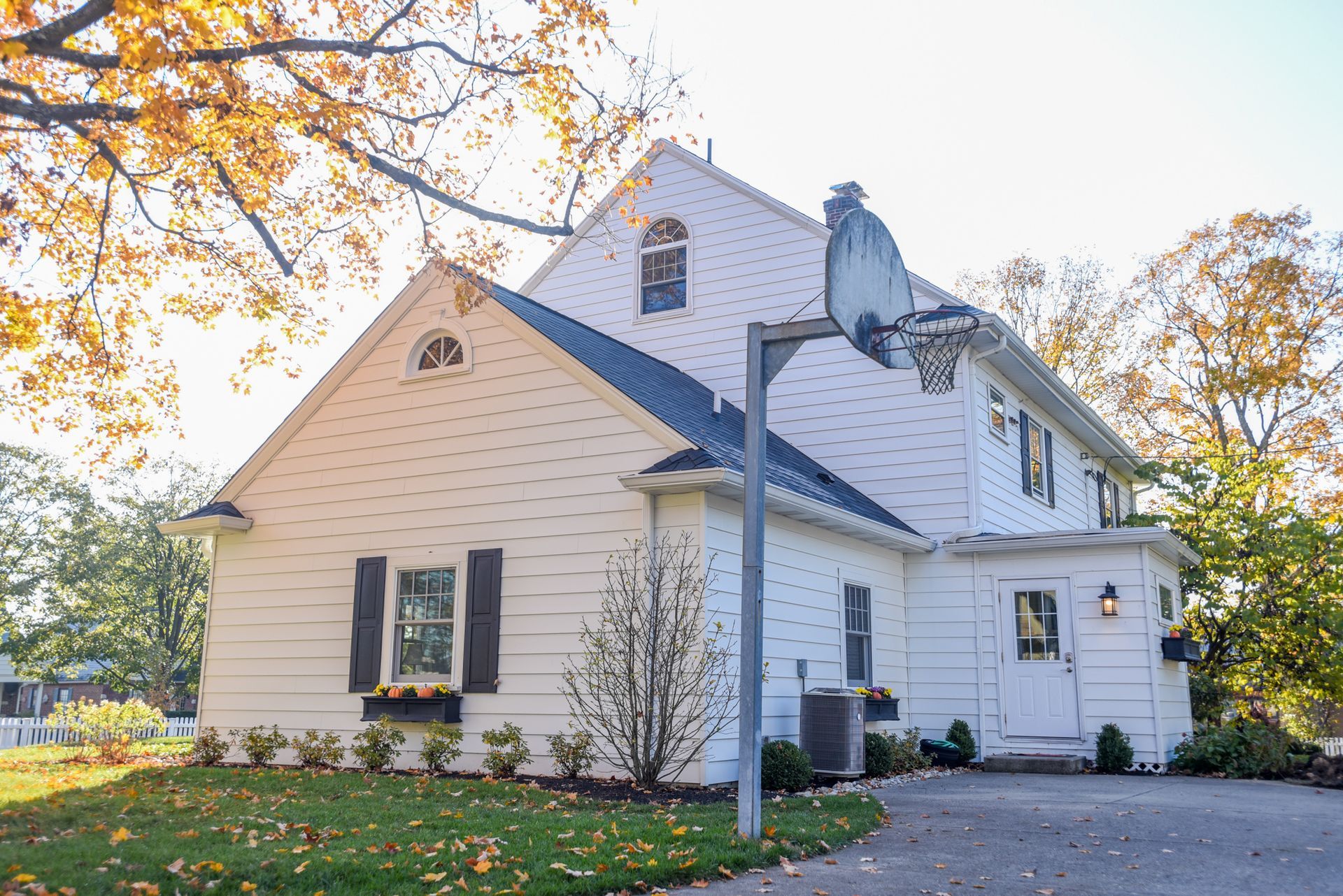 White house with blue shutters and a front porch, surrounded by autumn trees and a driveway.
