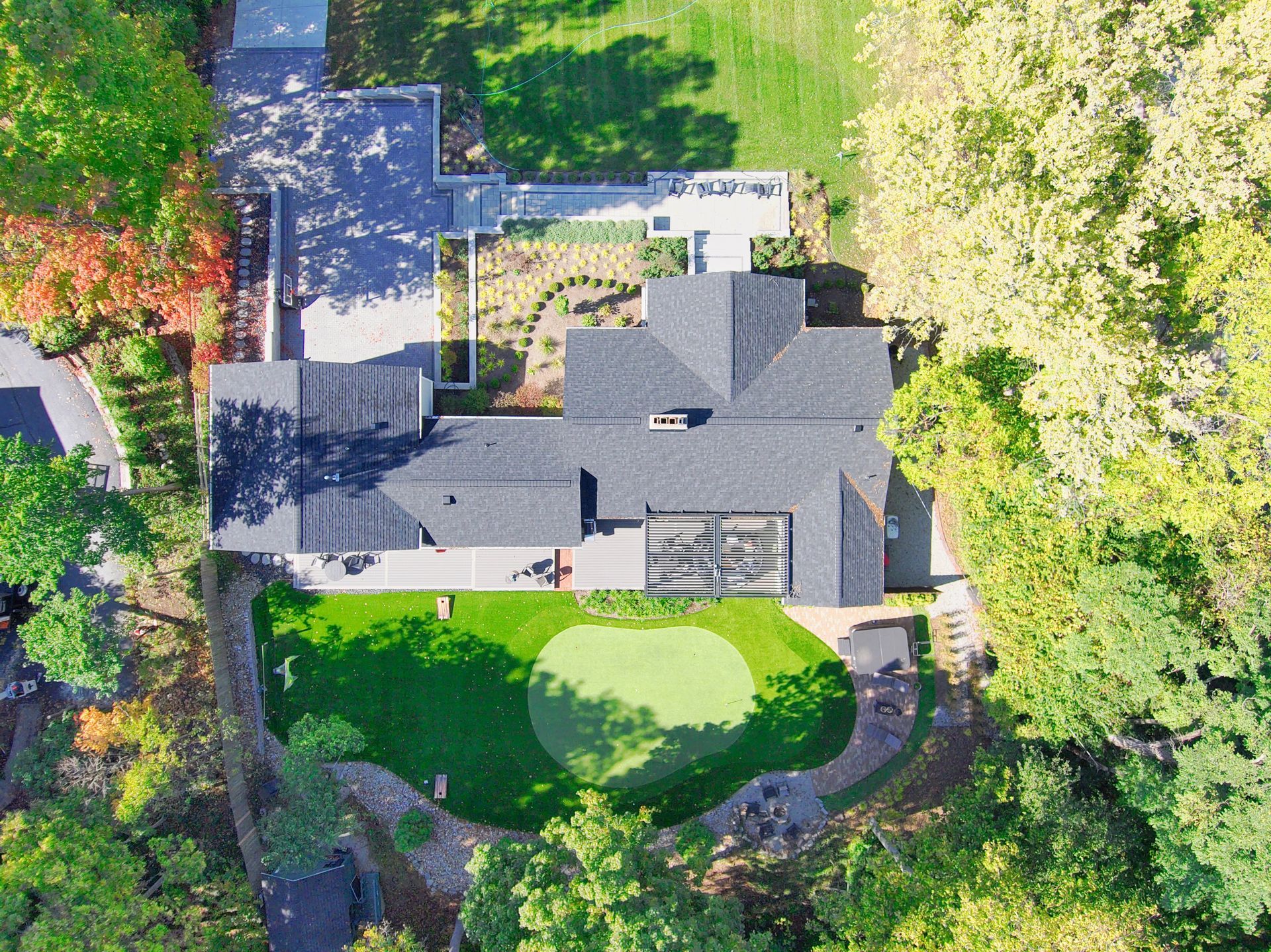Aerial view of a large house with a gray roof, surrounded by trees and a green backyard.