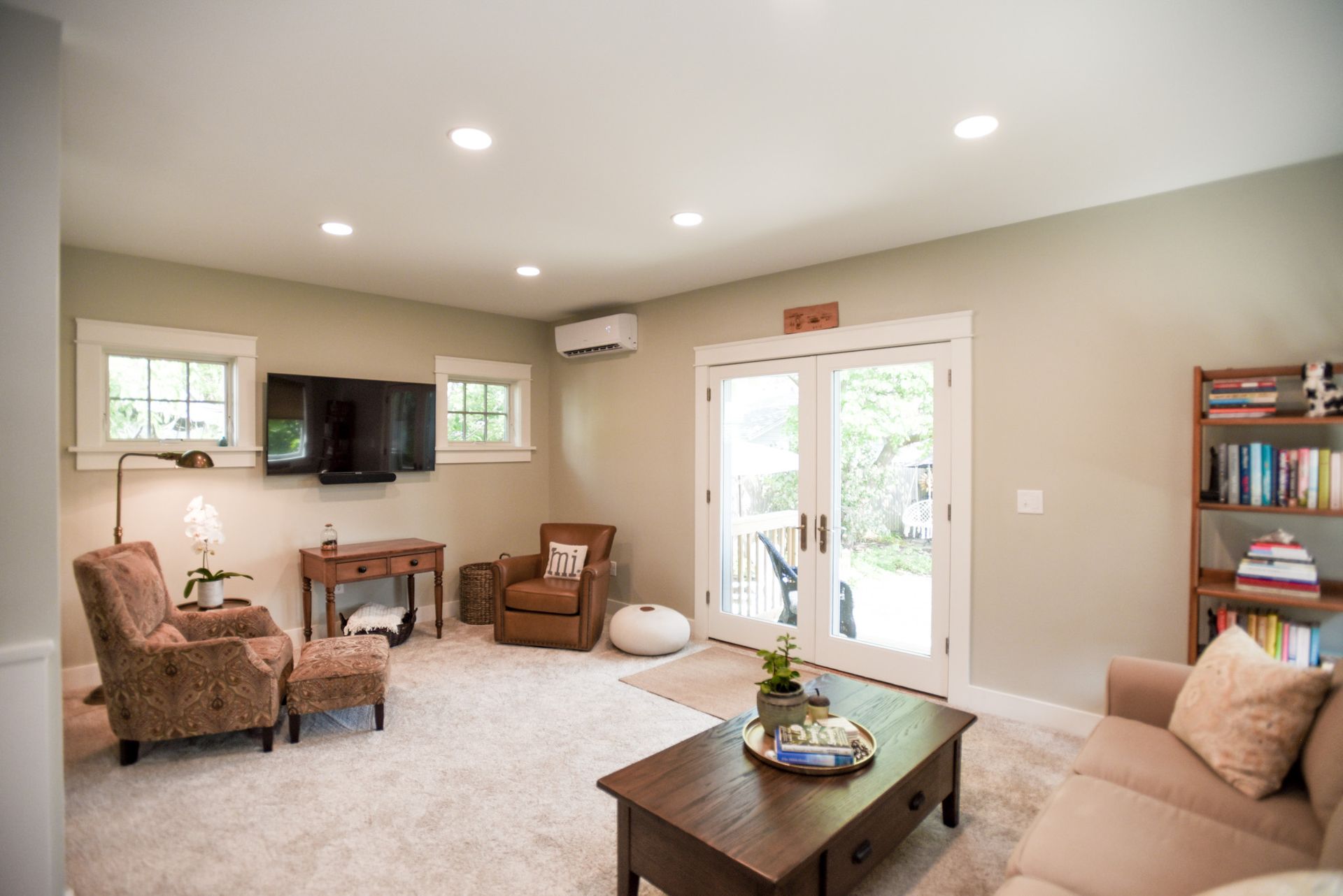 Bright living room with beige walls, carpet, sofa, chairs, coffee table, TV, and glass doors to the patio.