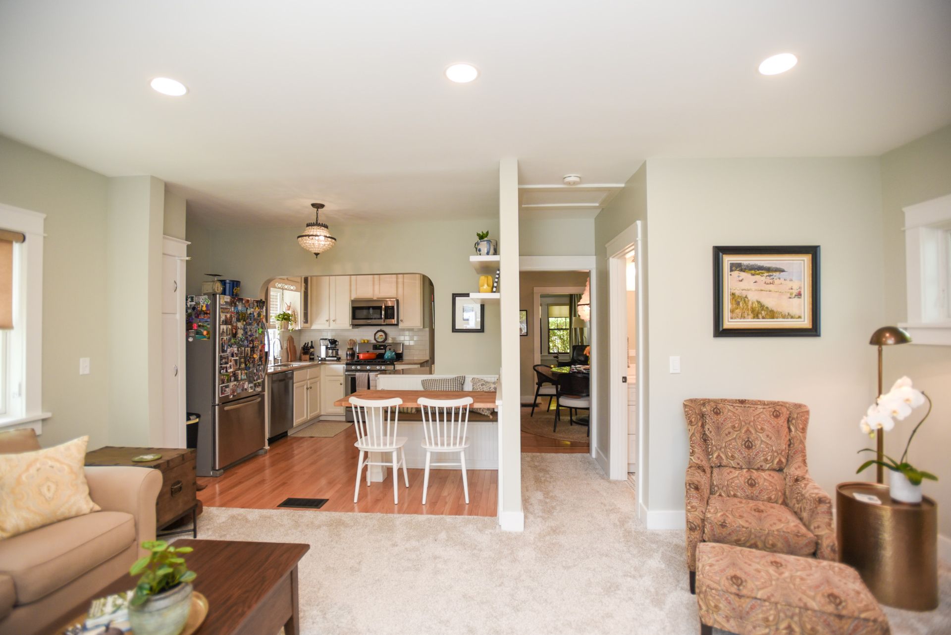 Open living-dining room with white table, beige furniture, and open kitchen in the background.