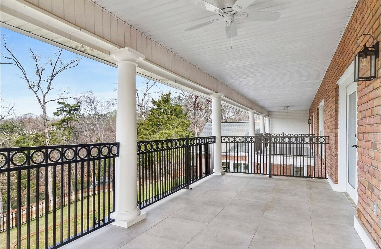 A large porch with a ceiling fan and a black railing.