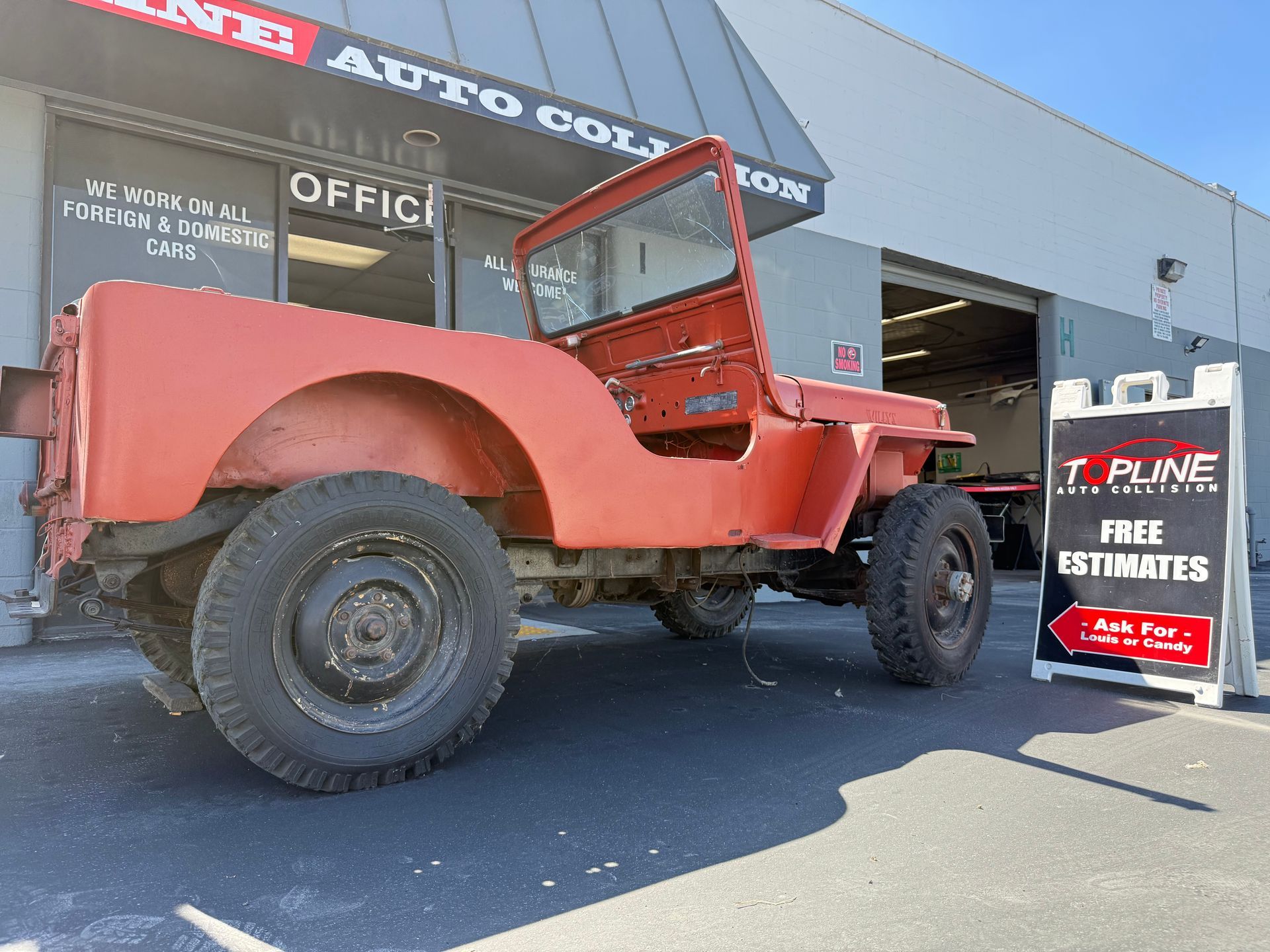 Red vintage Jeep parked in front of an auto shop.