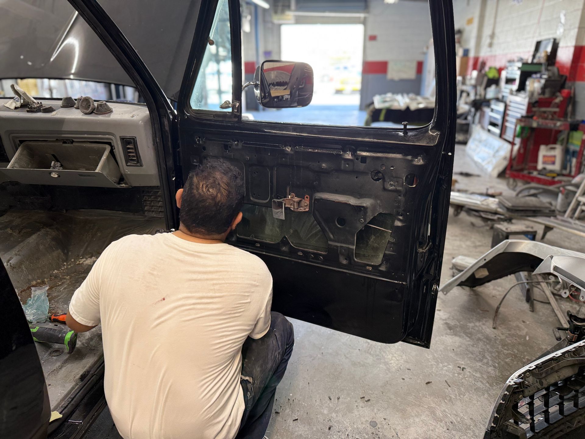 Person working on a black car door in a repair shop.