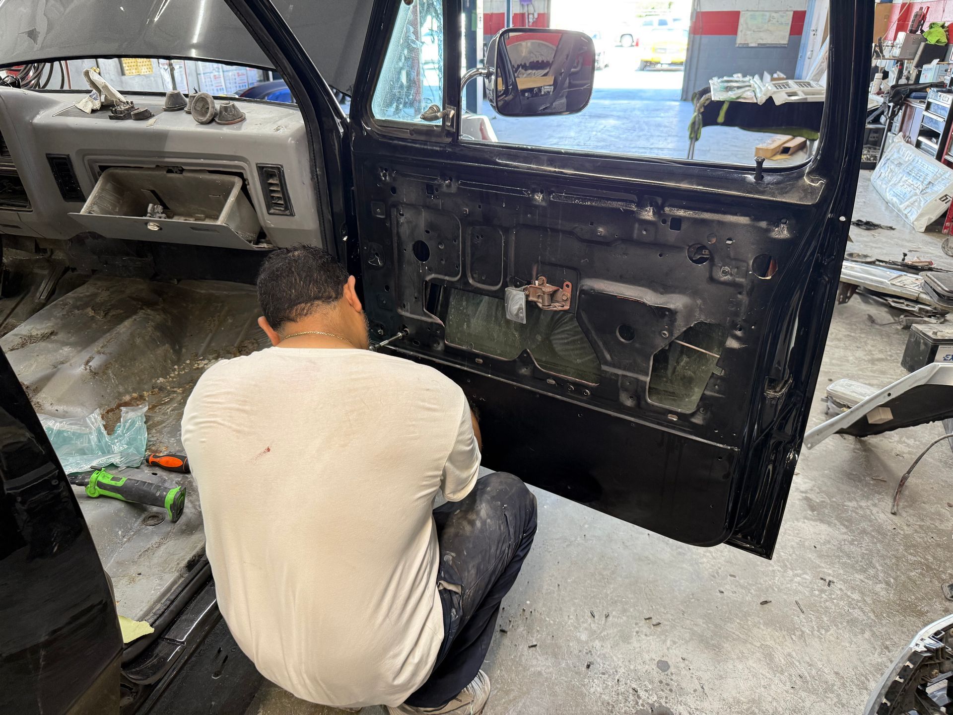 Person working on car door. Black vehicle, interior partially disassembled. Shop setting.