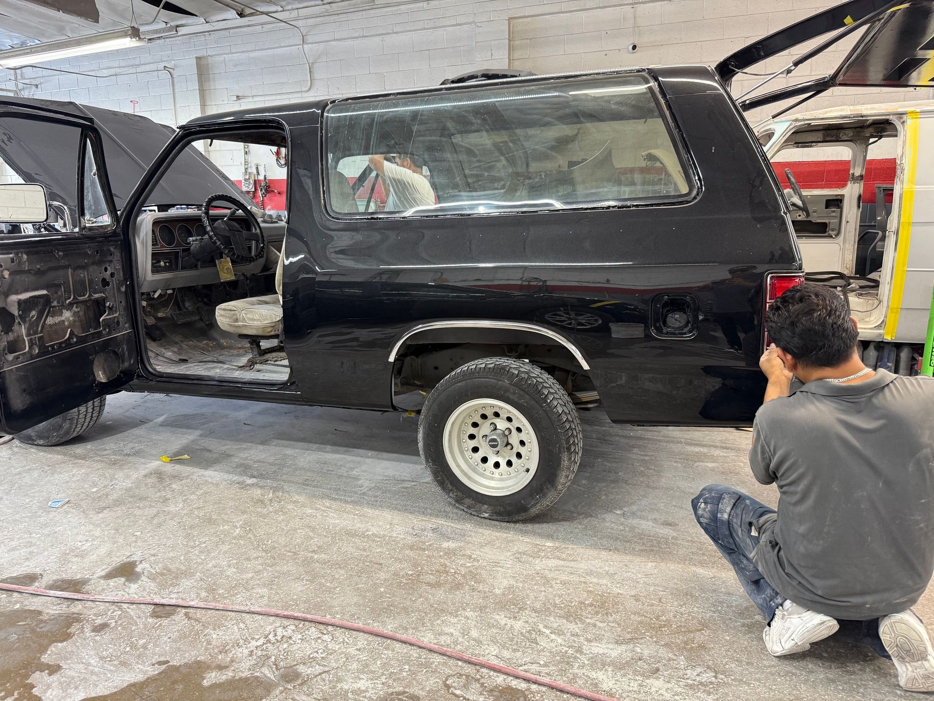 Man photographing a black SUV in a garage; doors open, interior visible.