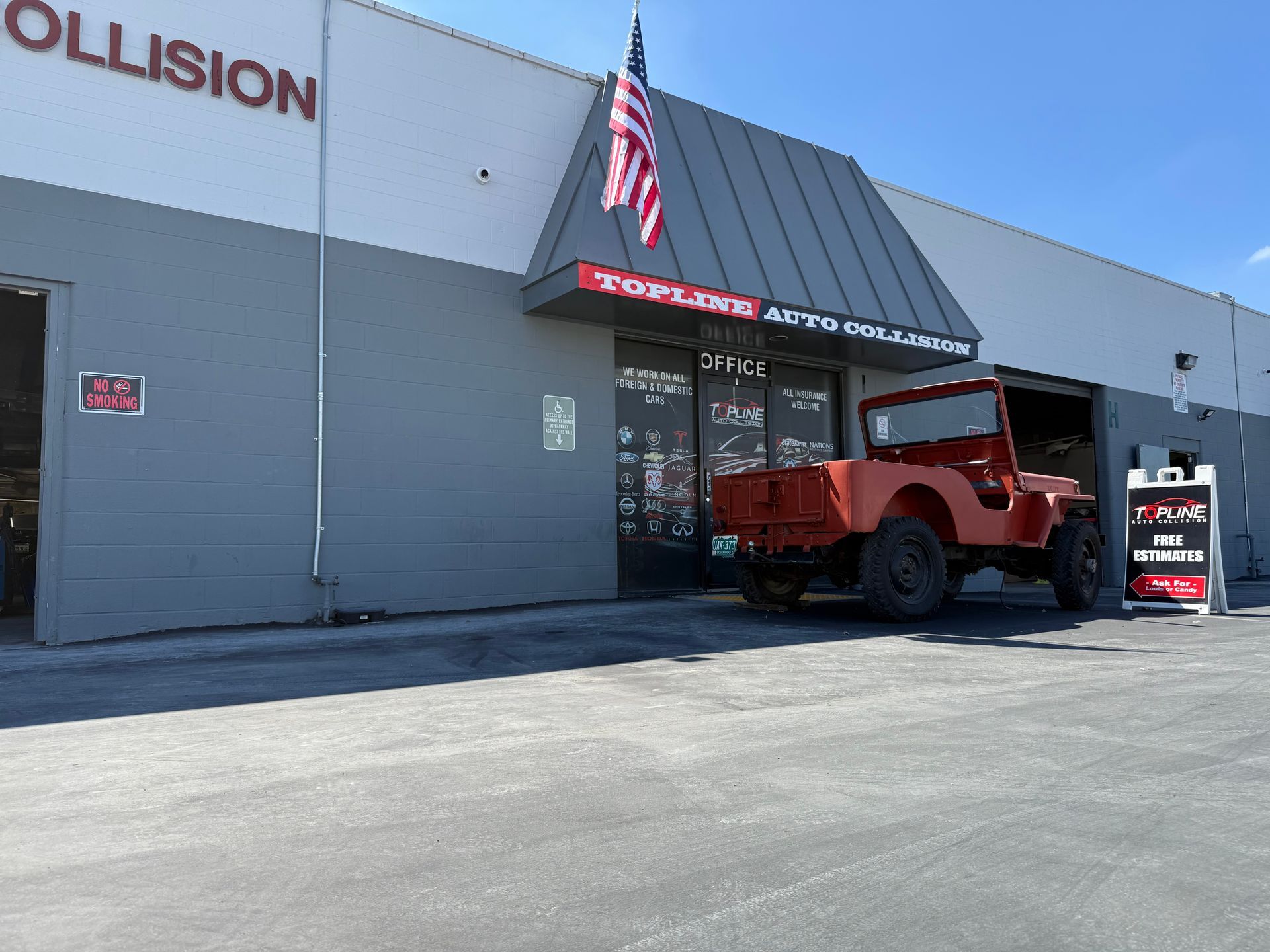 Red Jeep parked in front of a grey auto repair shop with an American flag.