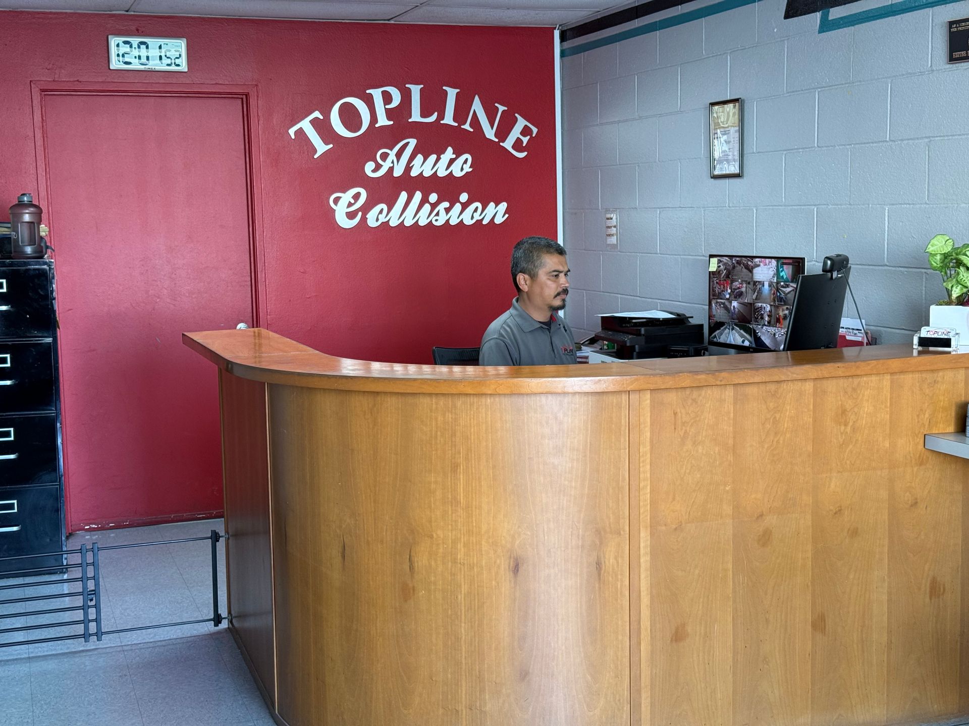 Man at the front desk of Topline Auto Collision. Wooden counter, red wall, and gray walls.
