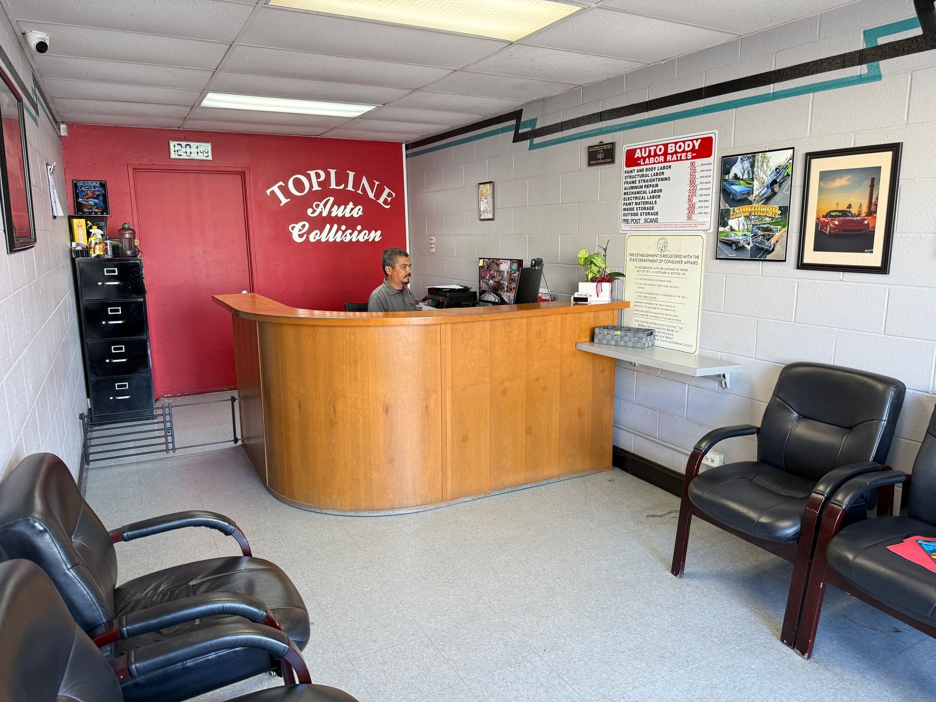 Reception area of Topline Auto Collision, with a person at the desk, waiting area with chairs, and signage on the walls.