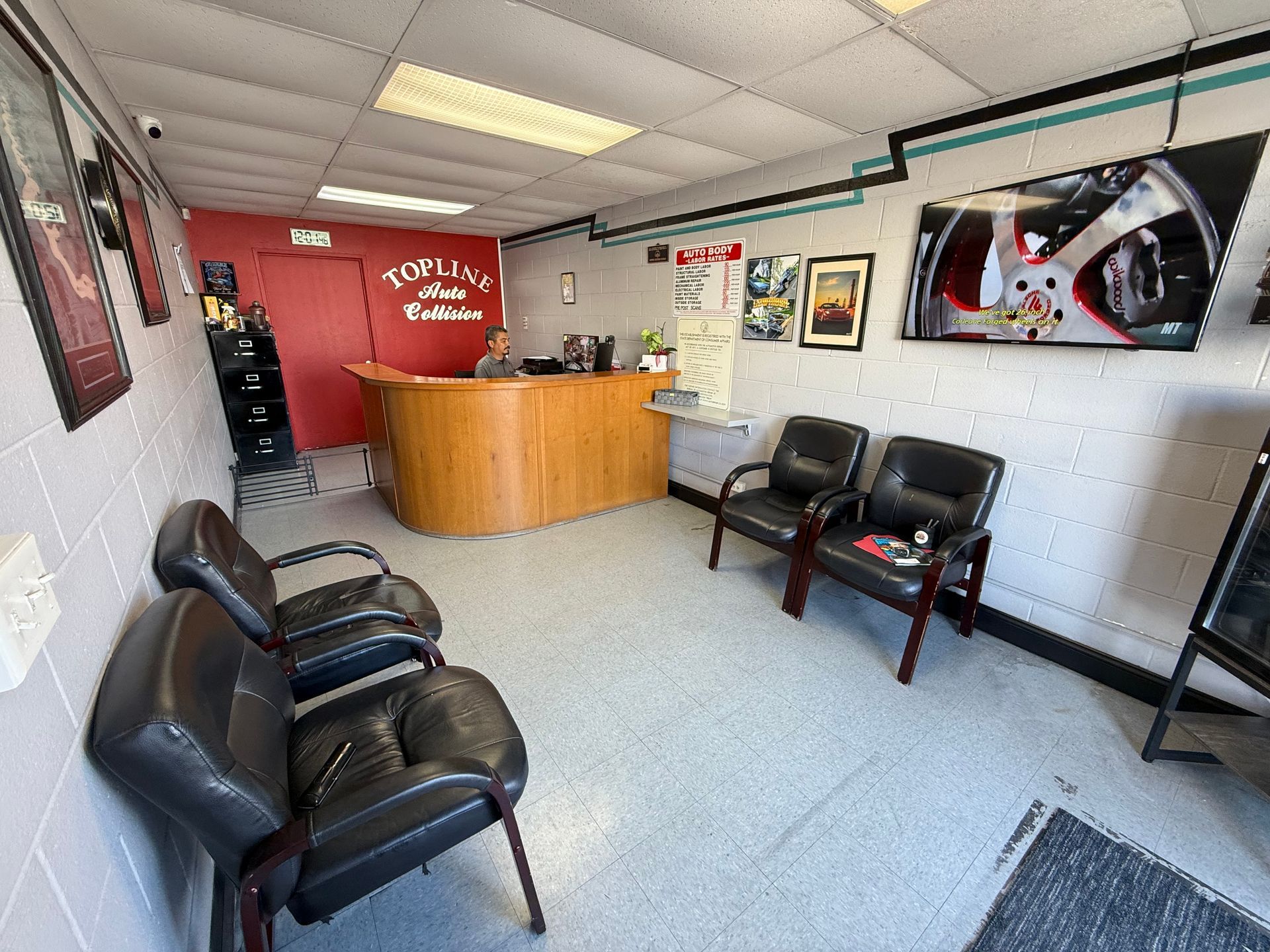 Waiting room with chairs facing a reception desk, art, and a TV screen, possibly at an auto shop.