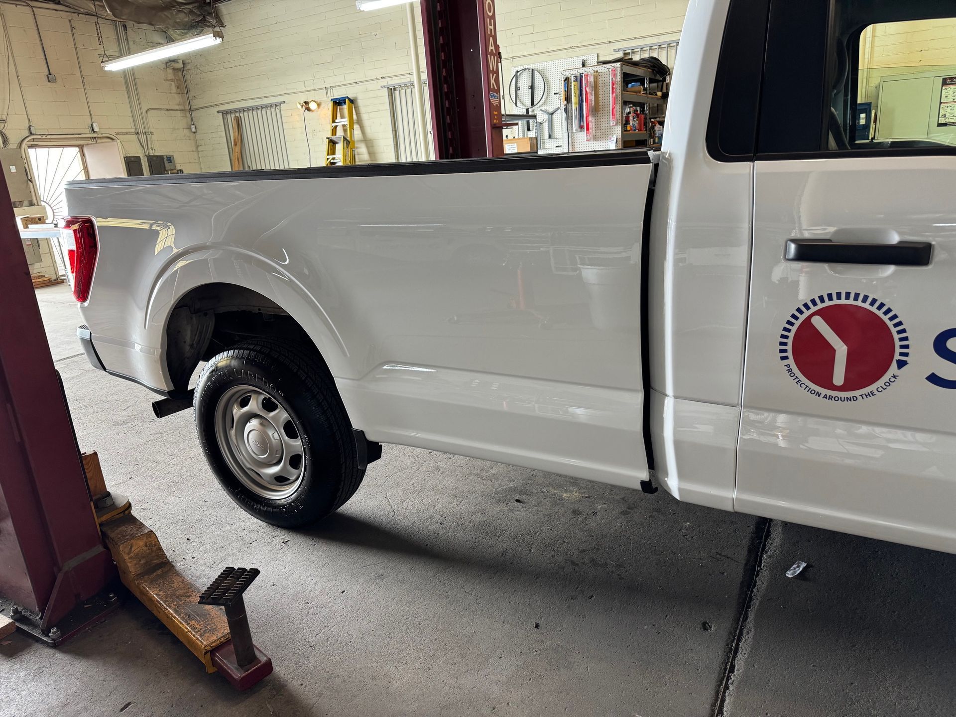 White pickup truck in a garage; side view with a company logo on the door.