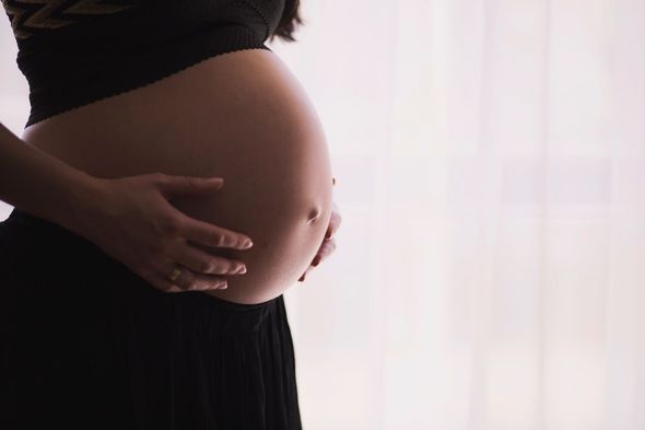 Pregnant person, side view, hands cradling large belly, dark clothing, bright background.
