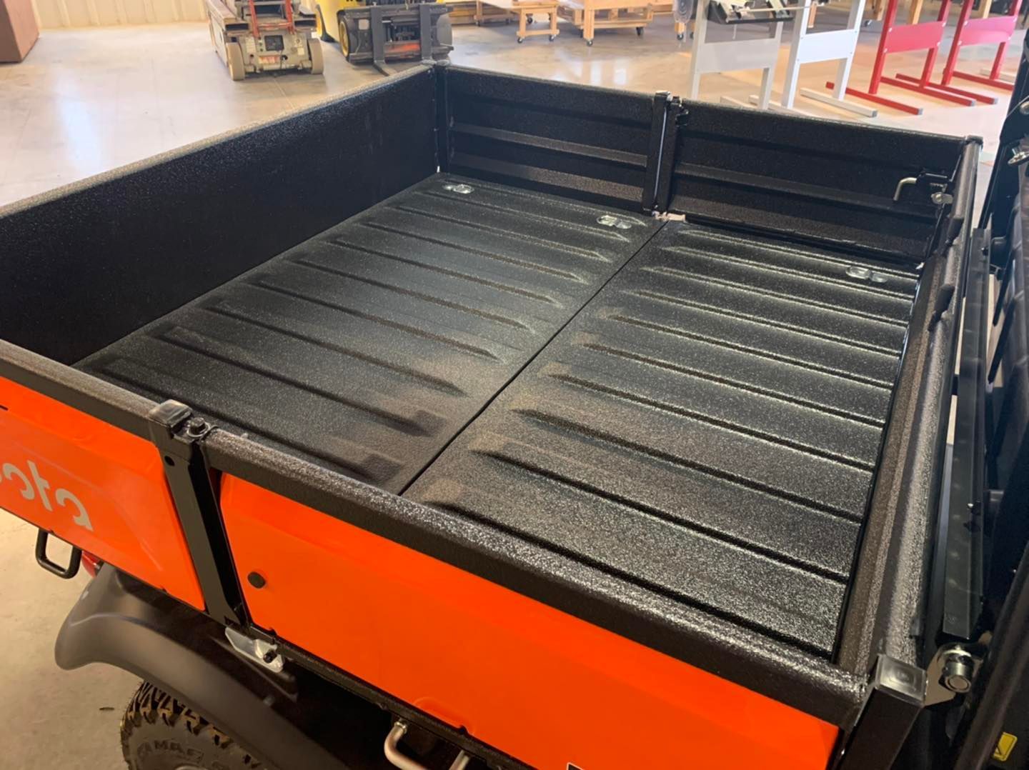 Orange Kubota utility vehicle bed, black textured surface.