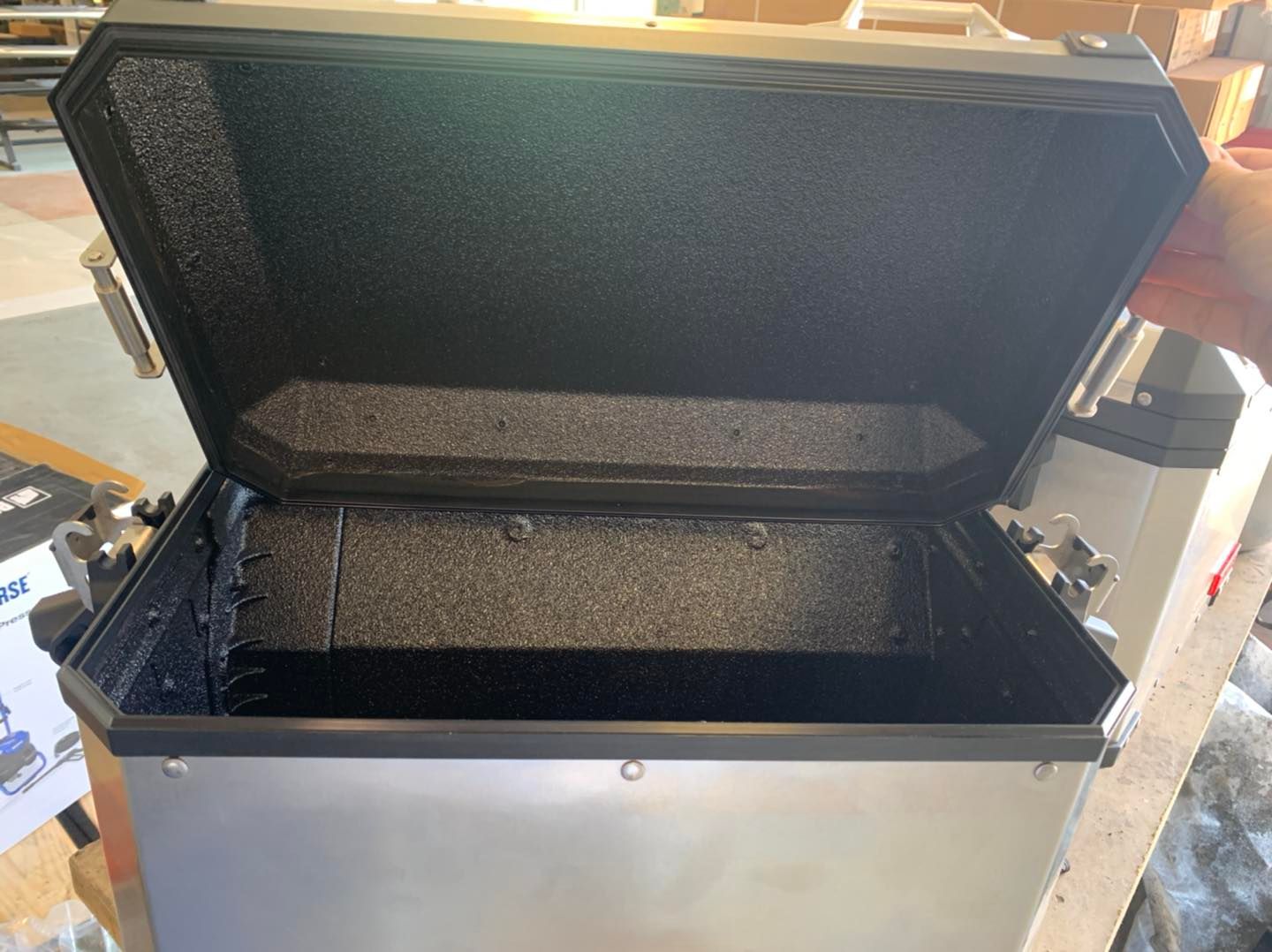 Open silver motorcycle side case with black interior and lid.
