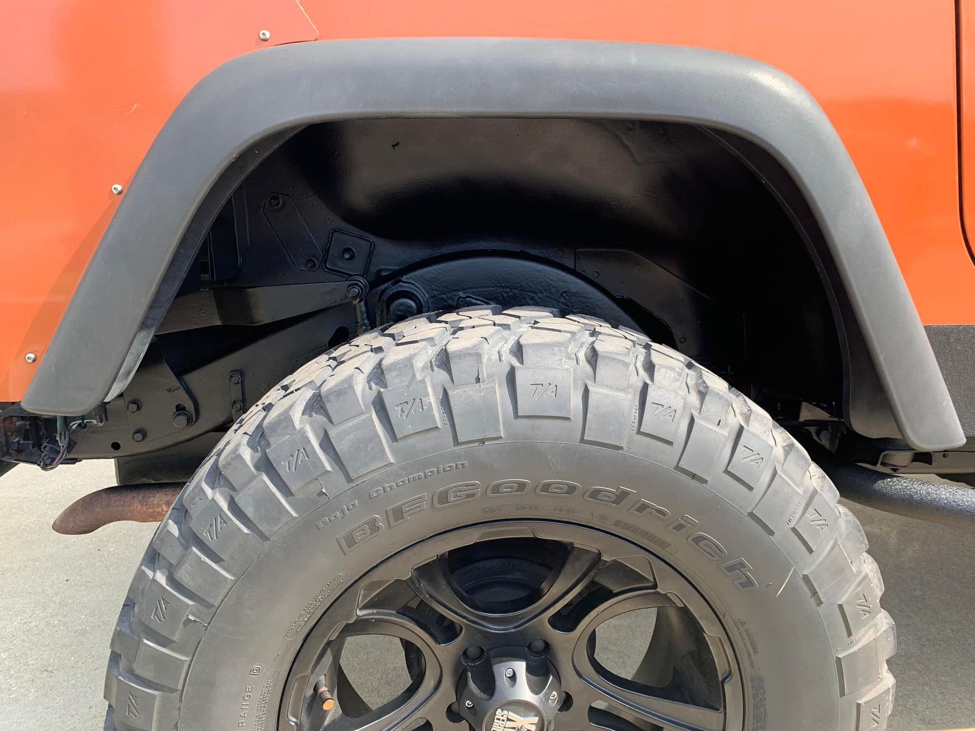 Black wheel well with tire and orange Jeep body.