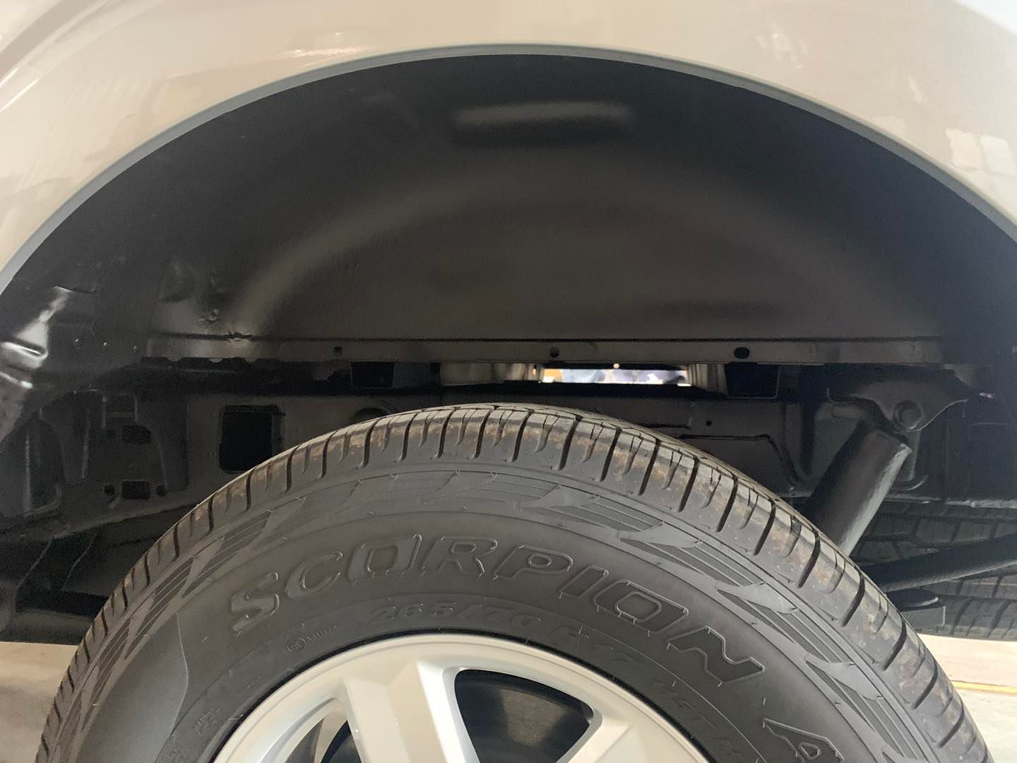 Close-up of a vehicle's rear wheel and wheel well. The tire is black with a silver wheel. The well is black.