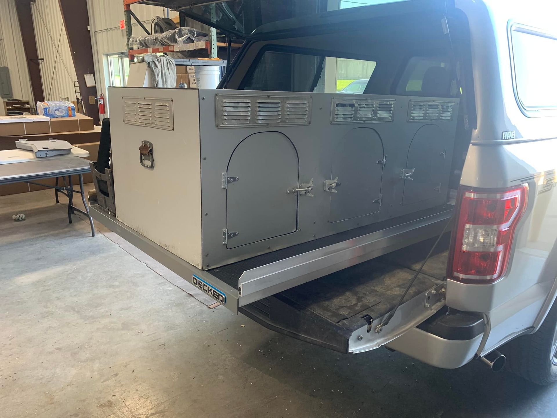 A truck bed with a light gray dog kennel installed on a slide-out tray.