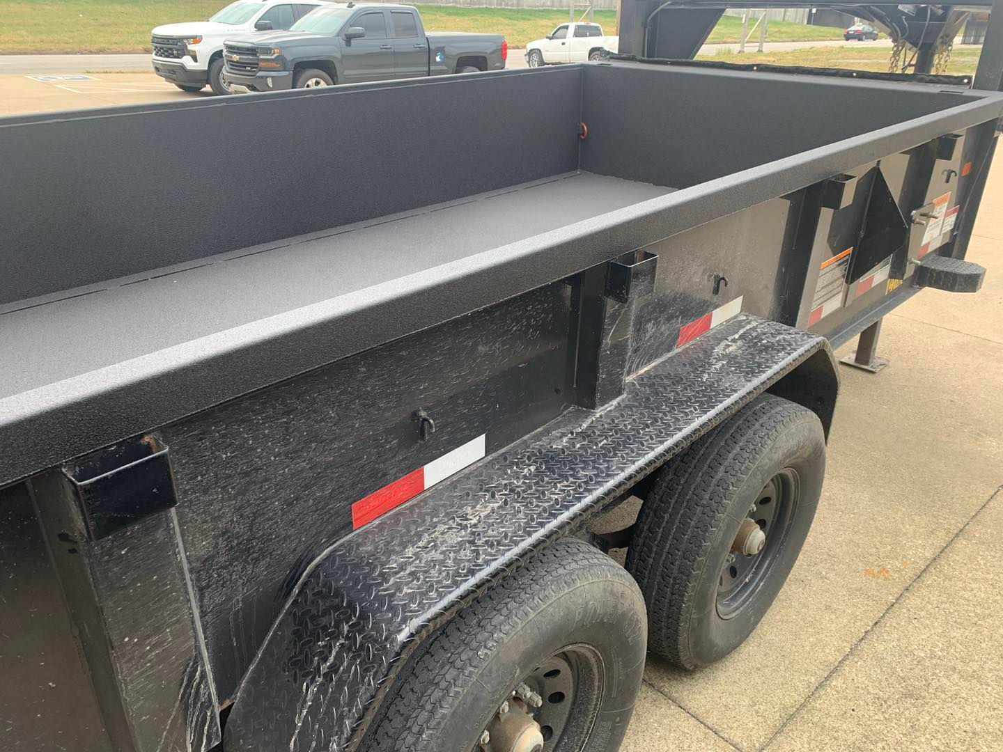 Black dump trailer with dual wheels, parked on asphalt.