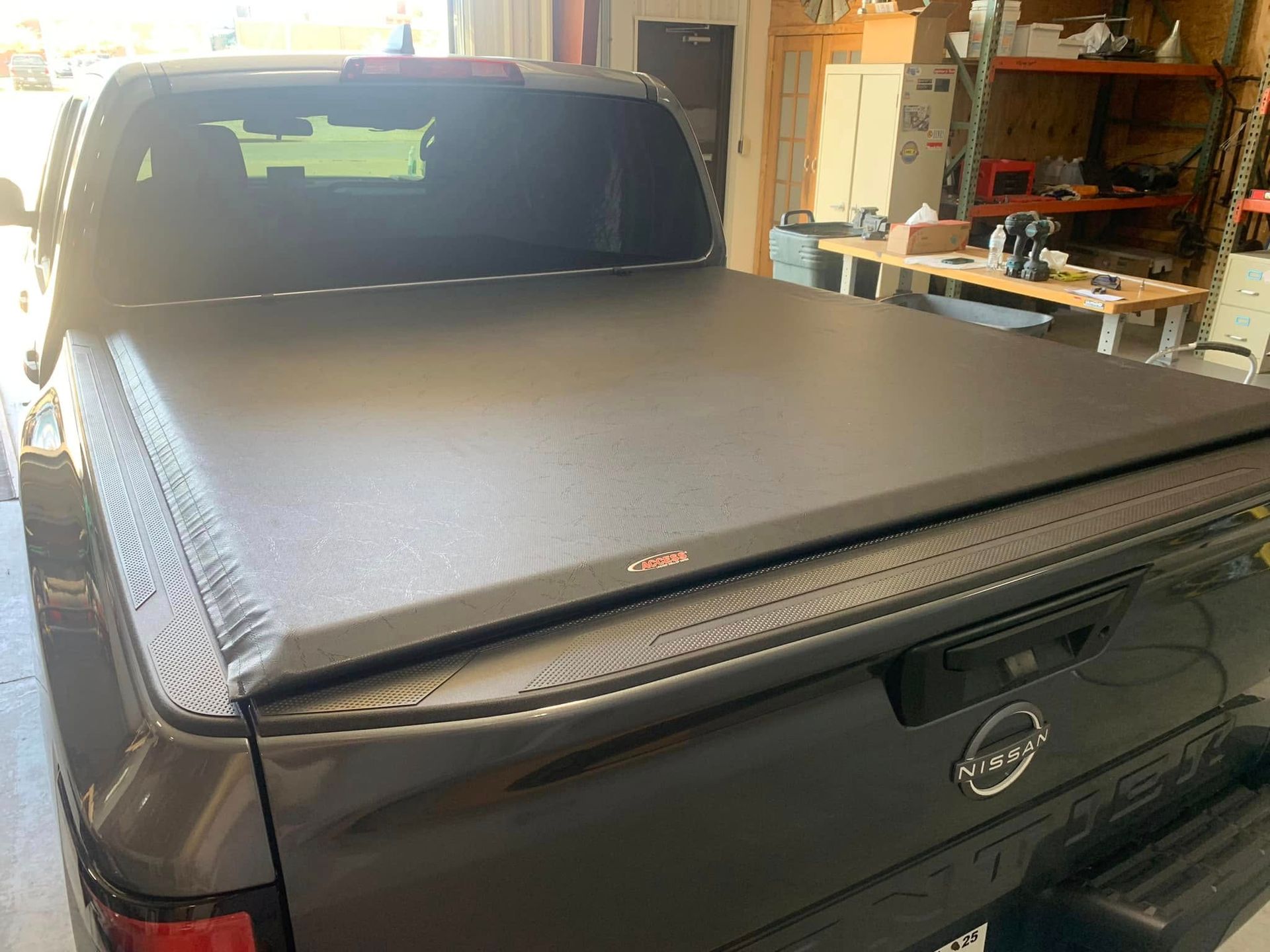 Black truck bed cover on a gray Nissan truck in a garage.