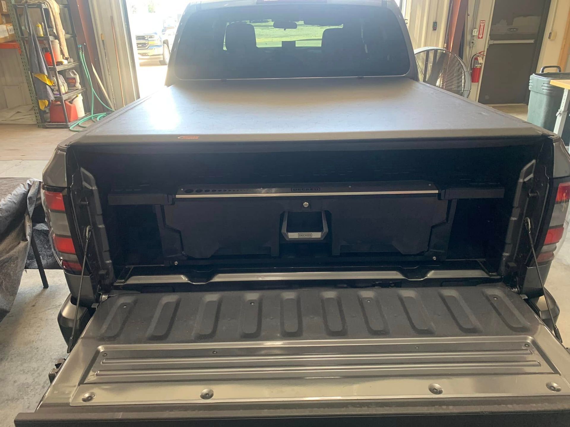 Black pickup truck bed with closed tonneau cover and drawer storage. Open tailgate.