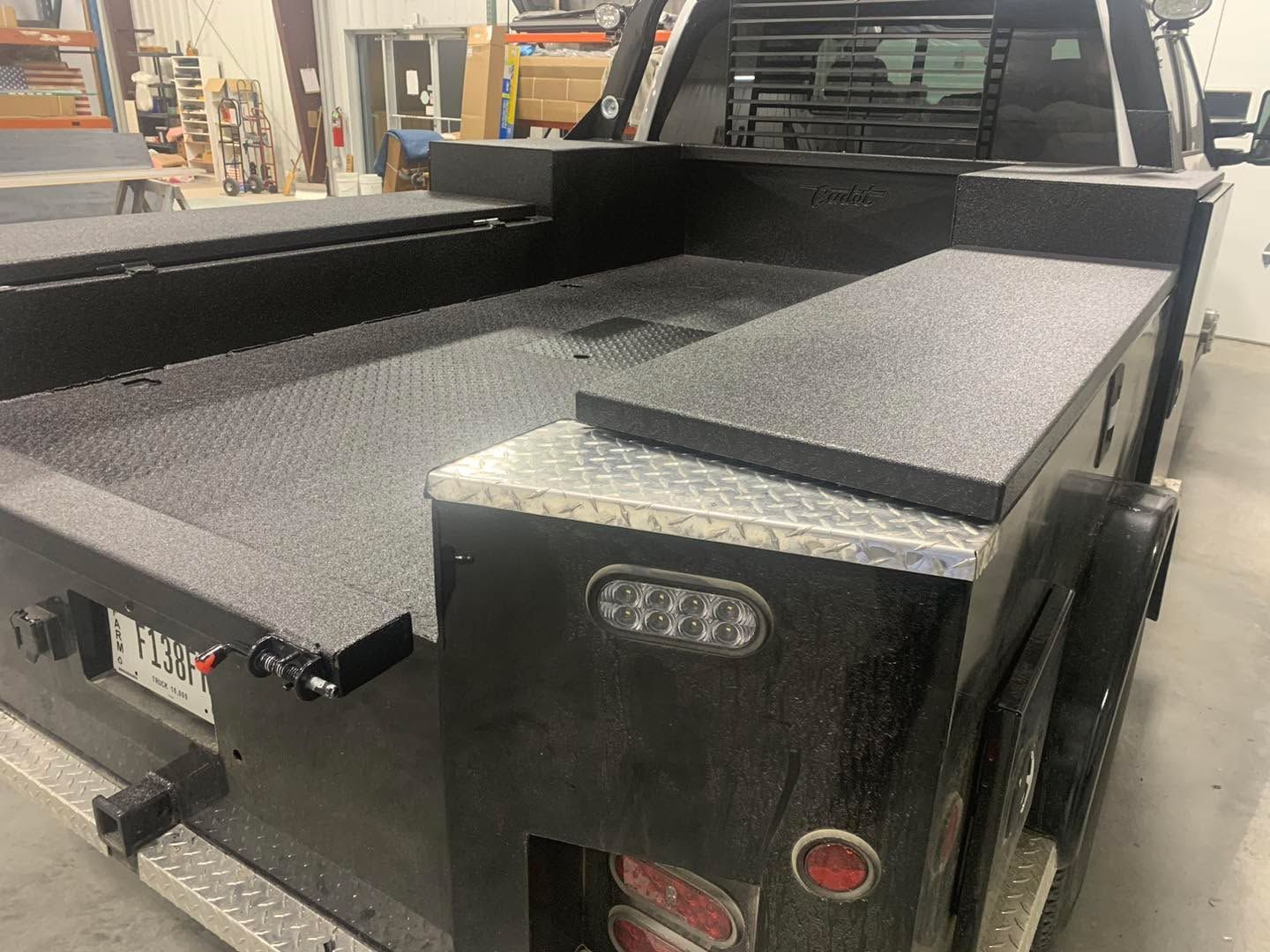 Black utility truck bed with storage compartments and textured surface.