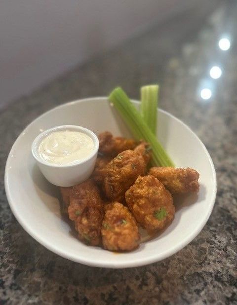 A bowl of chicken wings with celery and ranch dressing on a table.