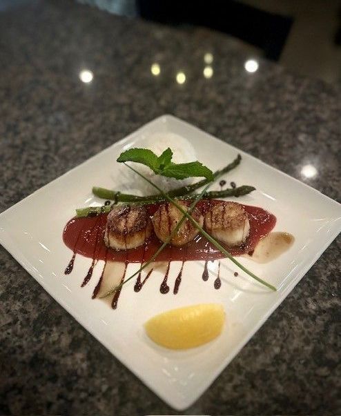A plate of food with scallops and asparagus on a table.