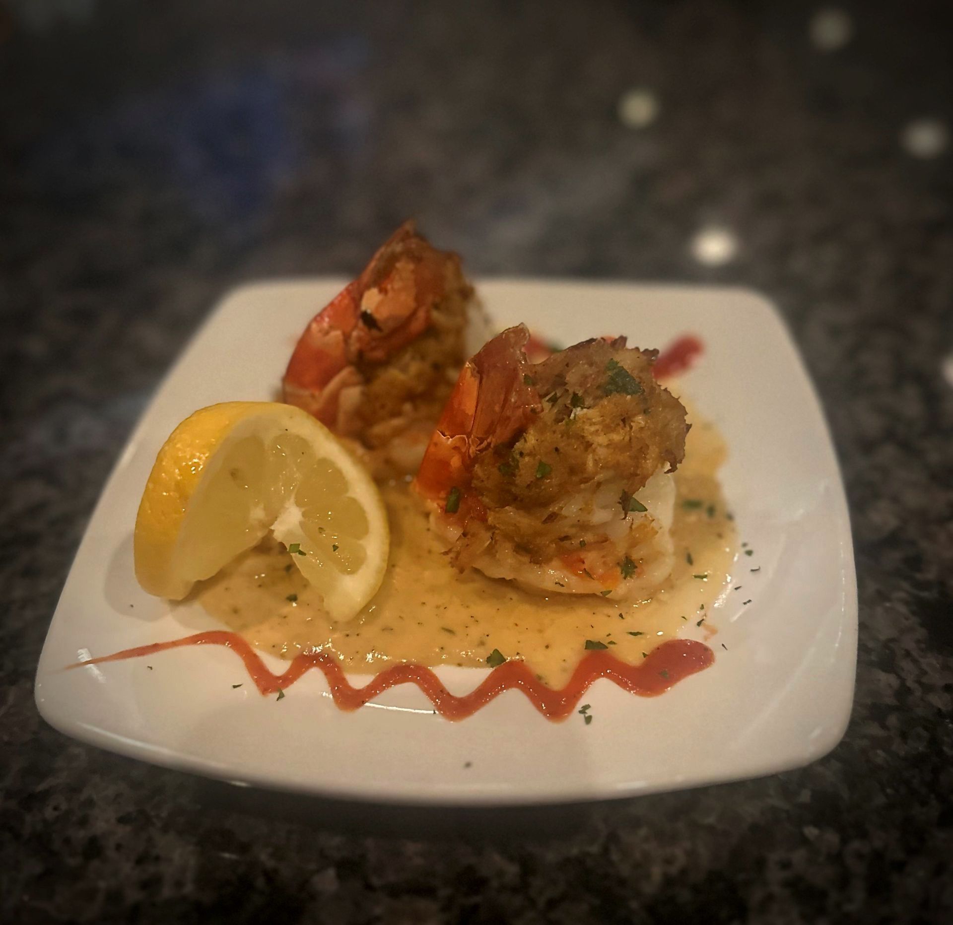 Stuffed shrimp with sauce and lemon wedge on white plate.