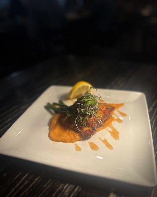 Grilled fish with asparagus, lemon wedge, and sauce on a square white plate.
