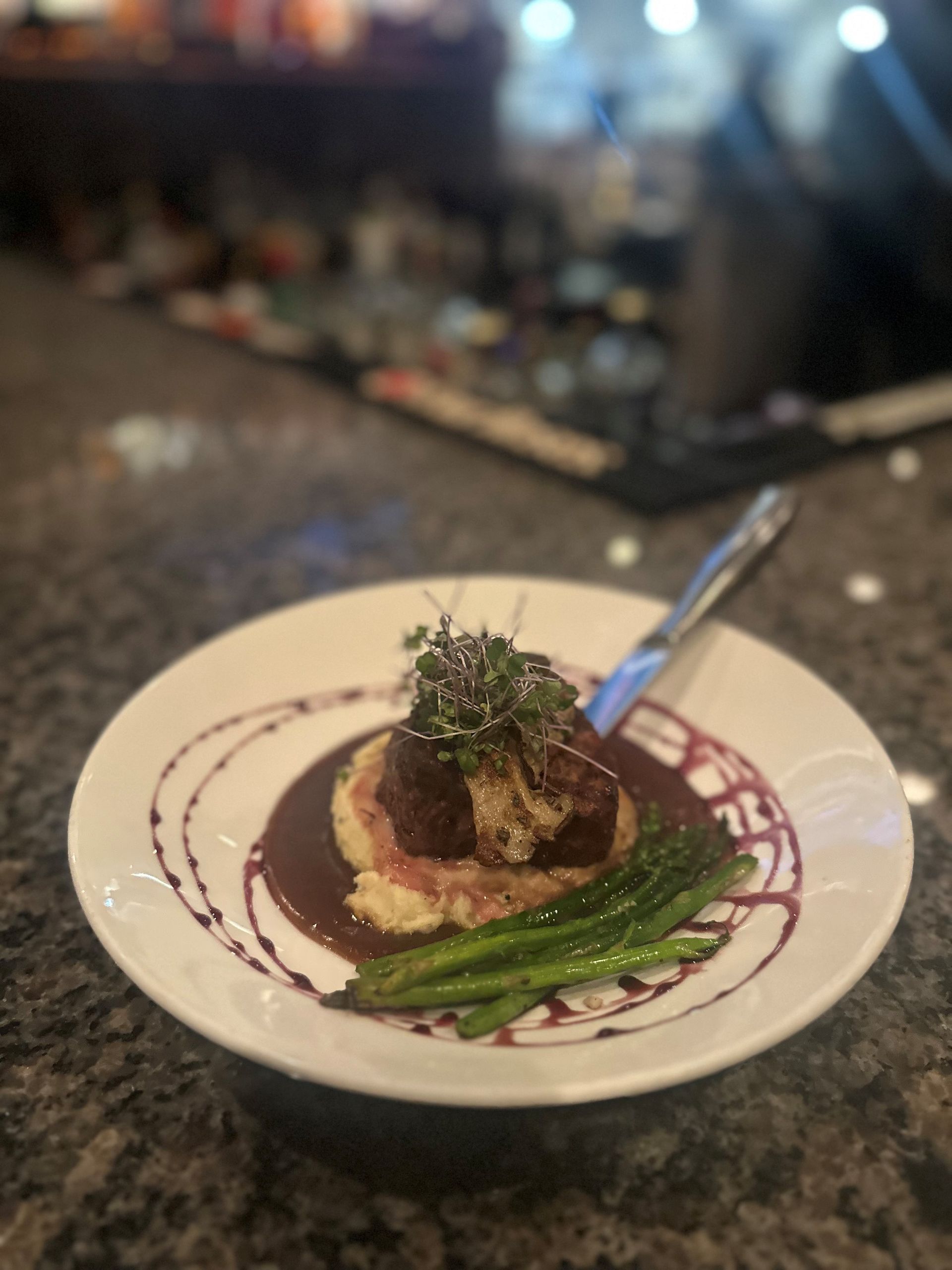 A plate of gourmet food featuring seared meat, asparagus, and sauce, on a blurred background.