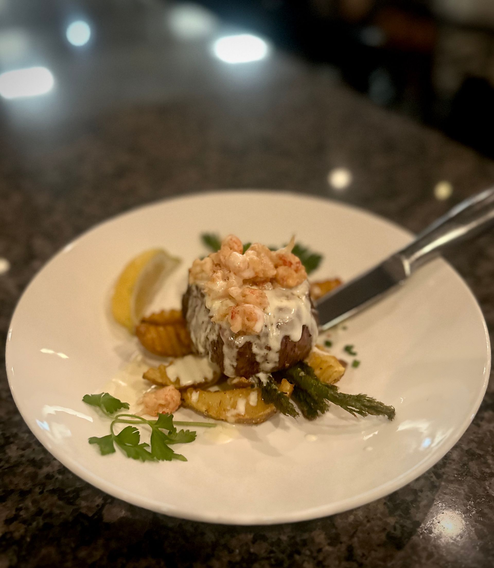 White dessert topped with whipped cream and nuts on a plate with fruit garnish and a spoon on a table