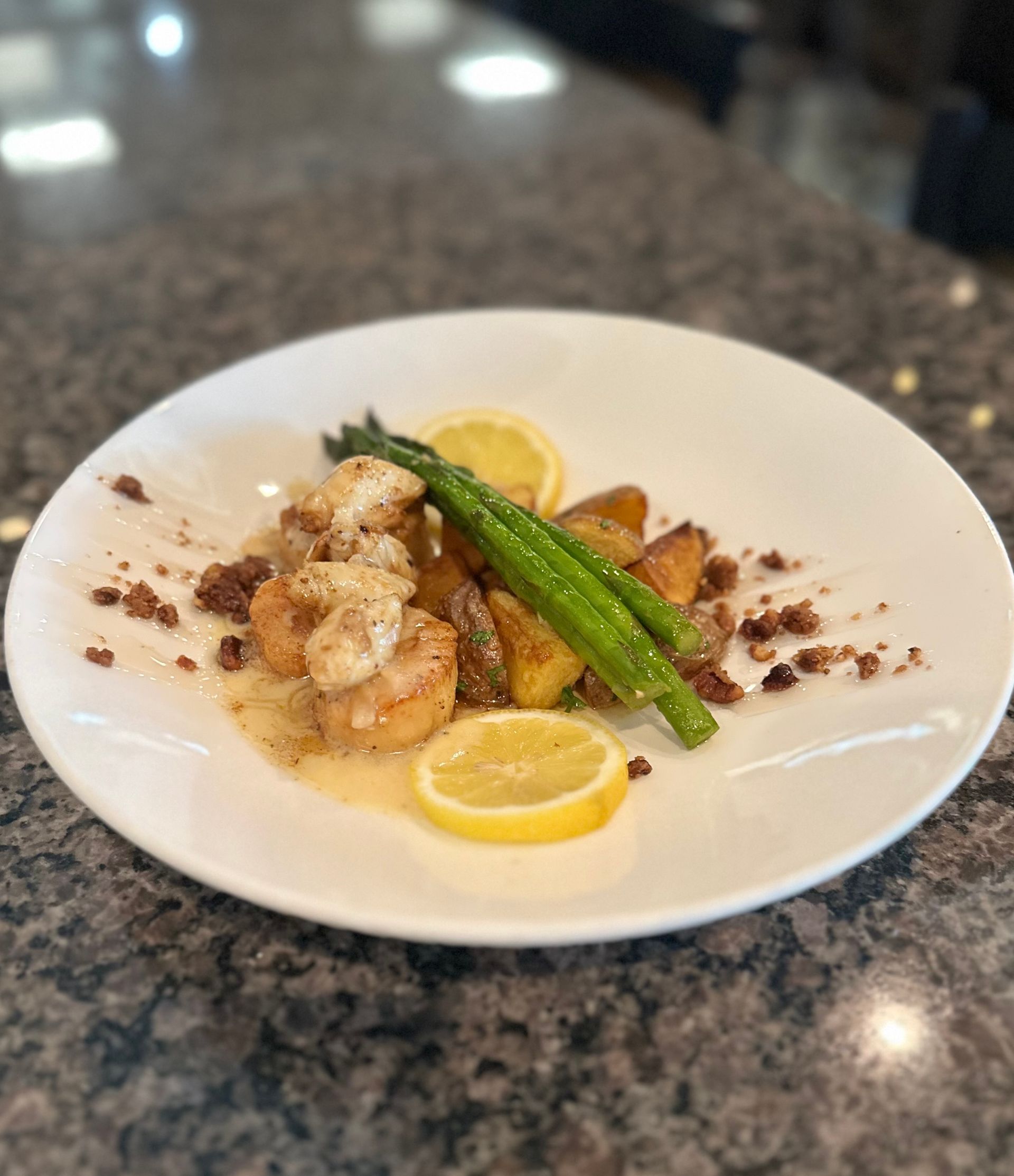 Plated seafood with asparagus and lemon on a white dish, served on a granite table.