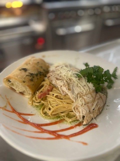 Plated pasta with shredded chicken, herb garnish, and red sauce drizzle on a white dish
