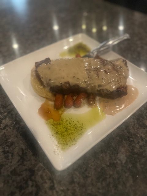 Plated seared meat entrée with vegetables and sauce on a white square plate
