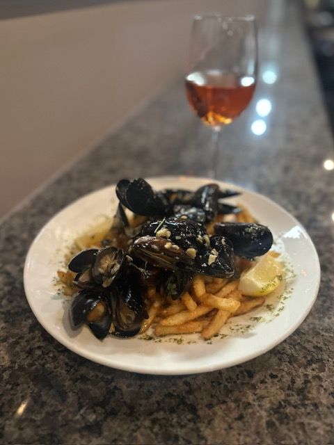 Plate of mussels and fries on a granite table, with a glass of red wine in the background