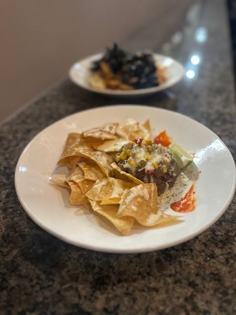 Two plated appetizers on a dark granite countertop, with crispy chips and a dark topping in the foreground.