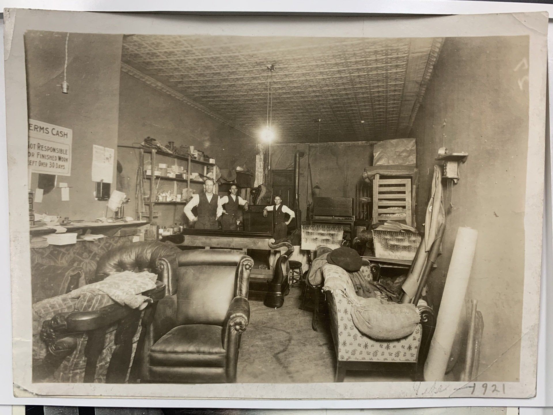 Crowded vintage furniture store with upholstered chairs, shelves, and people working in the back room