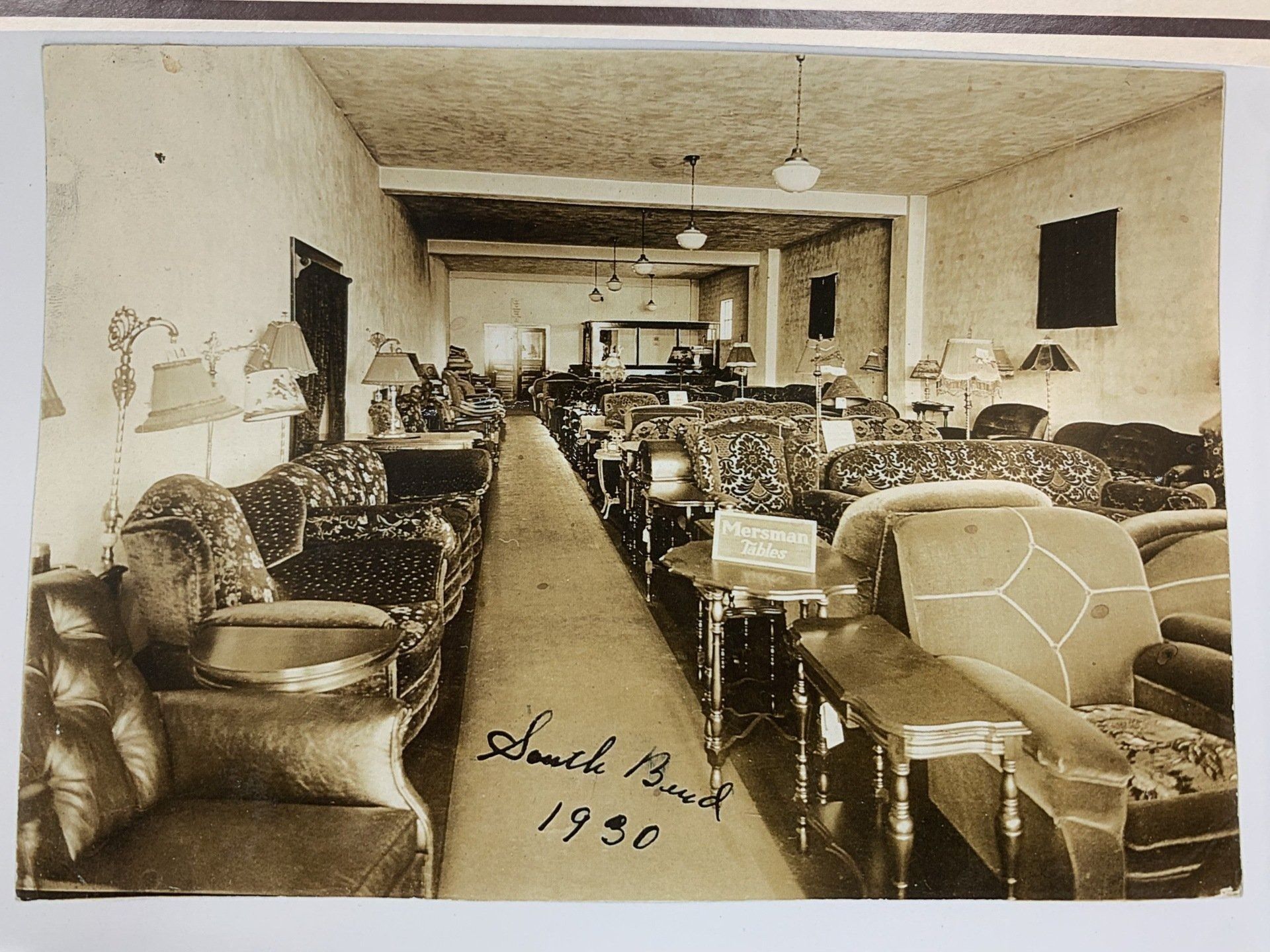 Sepia-toned antique store with rows of chairs and sofas, handwritten “1930” at bottom.