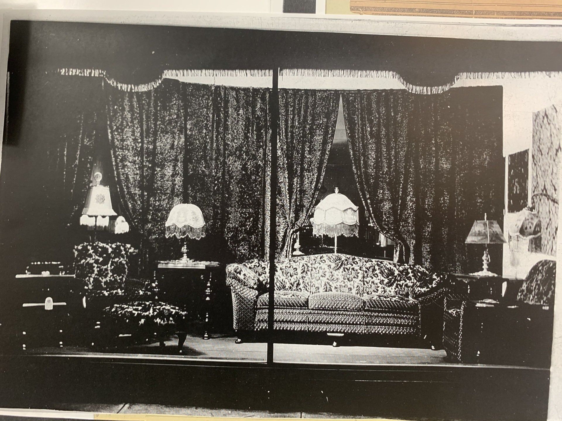 Black-and-white bedroom interior with a bed, draped curtains, and two lamps on side tables.