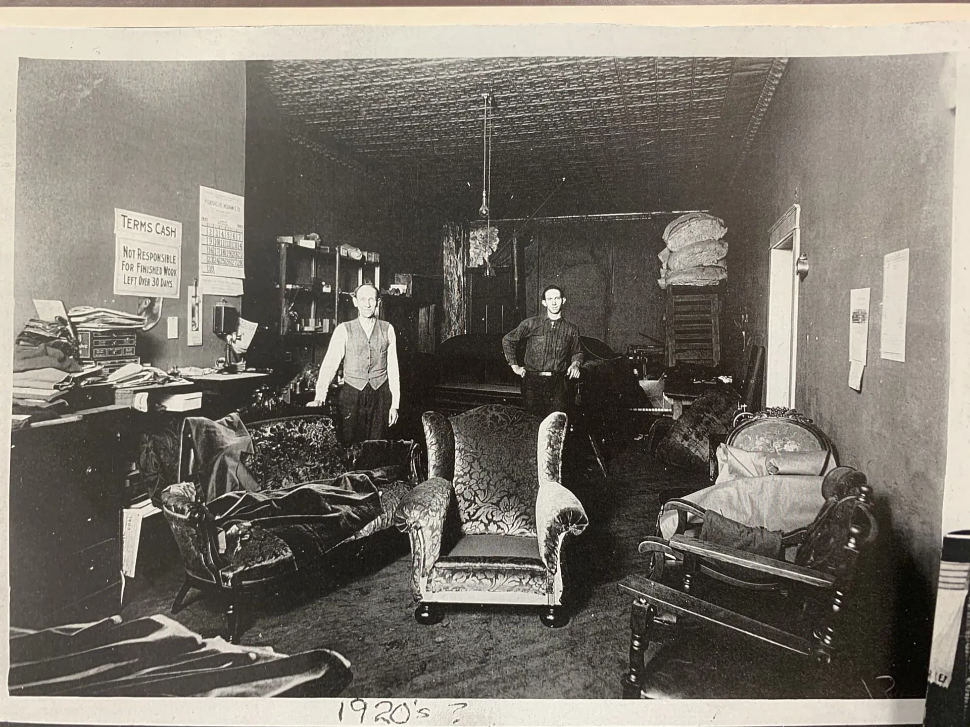 Old-fashioned living room with ornate chairs, table, and a person standing in the background.