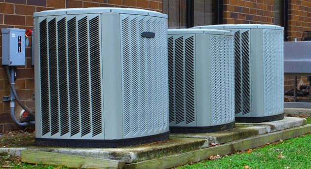 Three large outdoor HVAC units with gray metal grilles on a concrete pad beside a building.