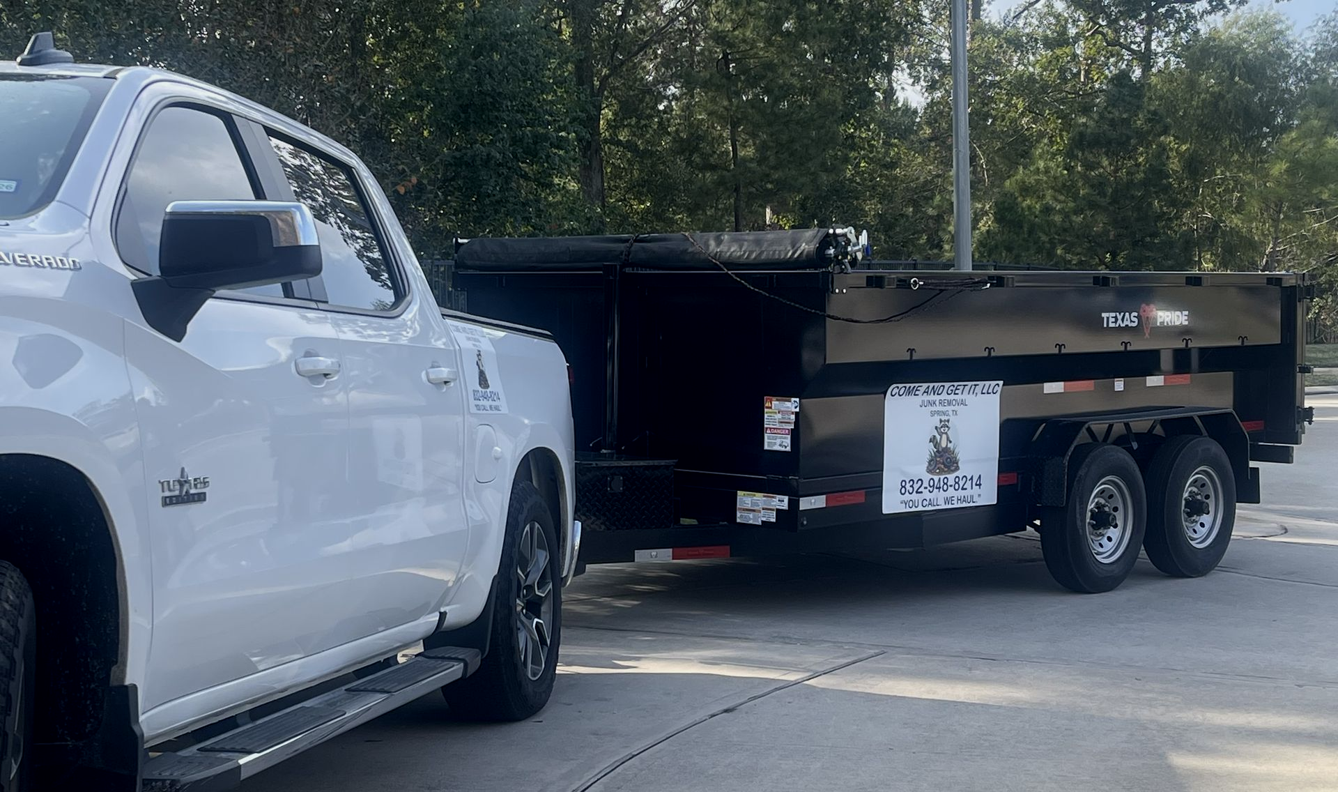 White pickup truck hitched to a black dump trailer, parked outdoors.