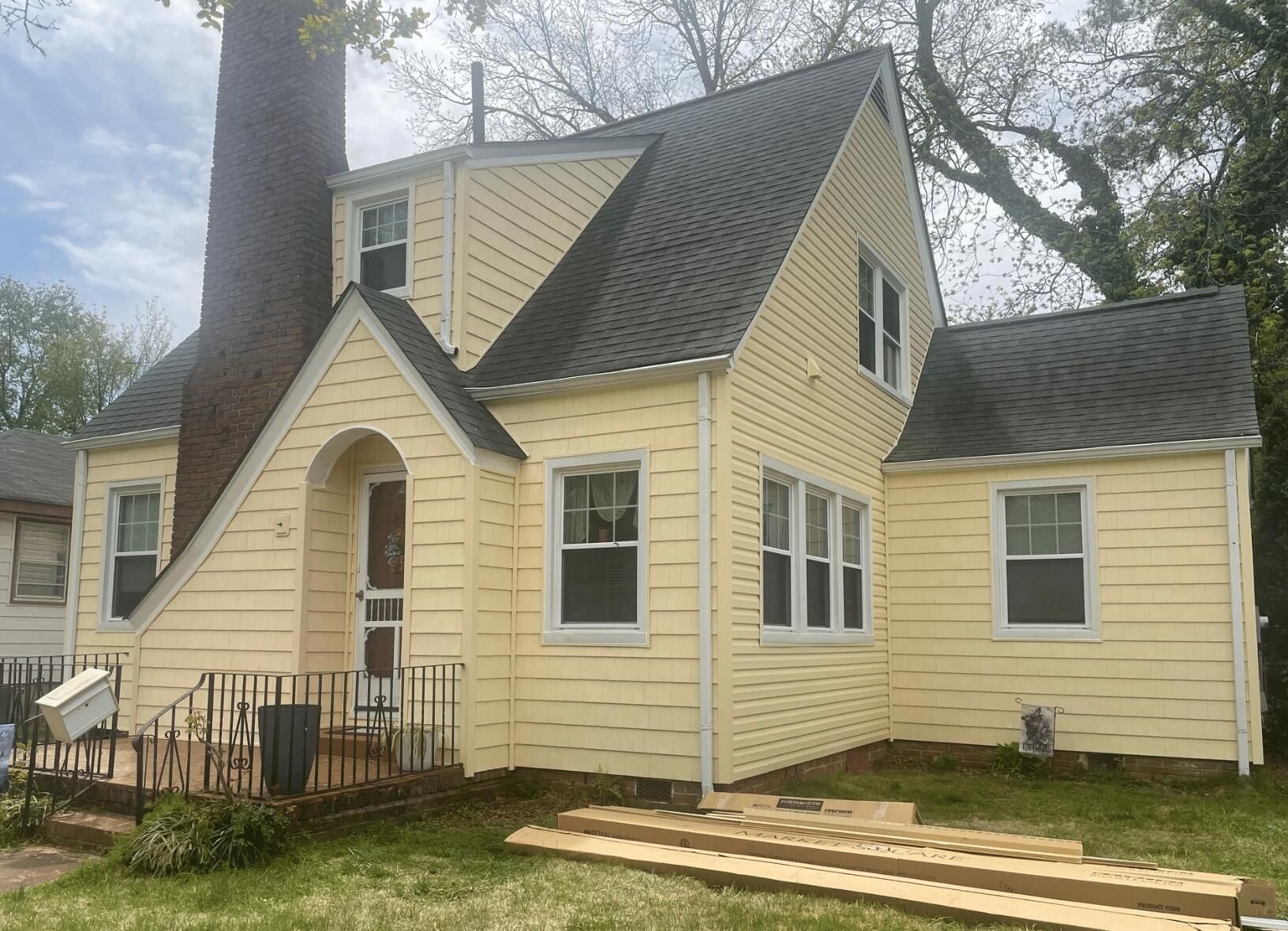 A yellow house with a black roof and white windows