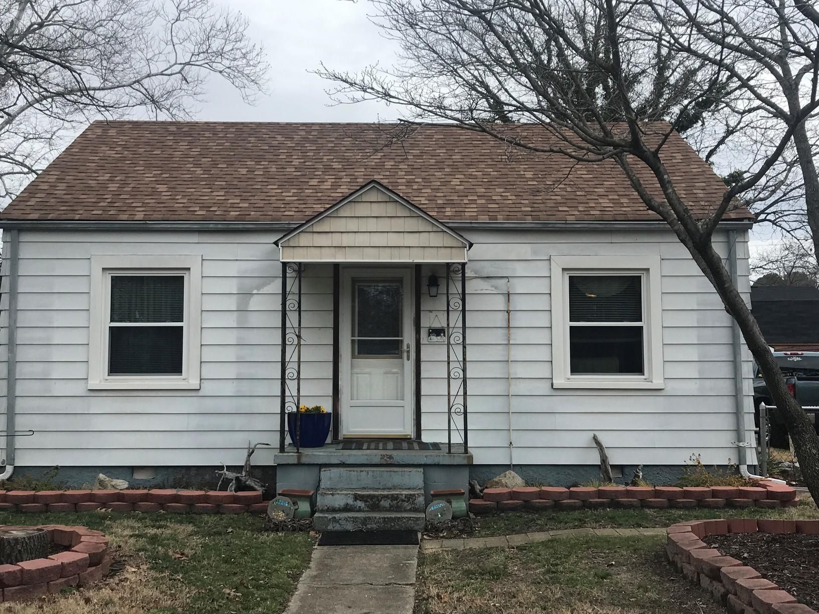 A small white house with a brown roof and a porch.