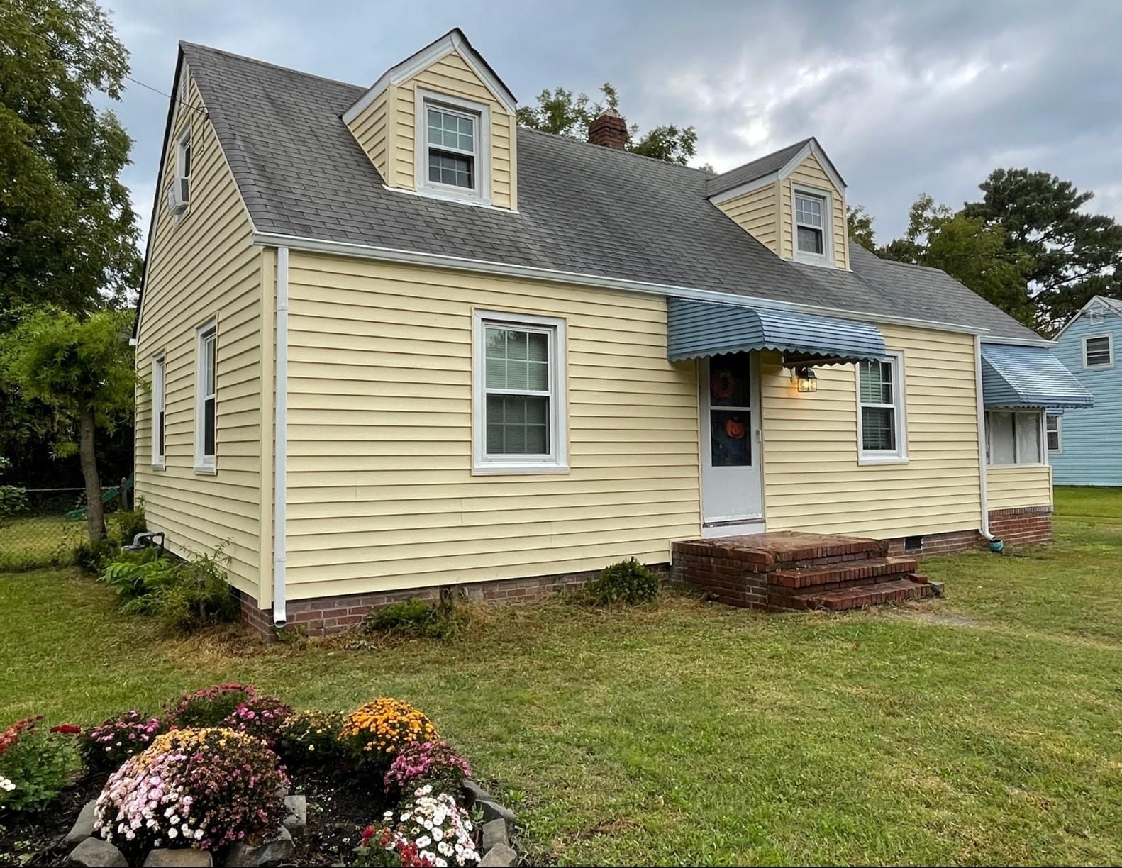 A yellow house with a gray roof is sitting on top of a lush green field.