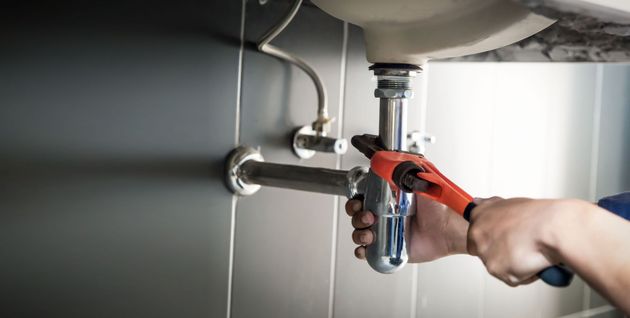 Person using pliers to tighten a sink drain pipe under a bathroom sink