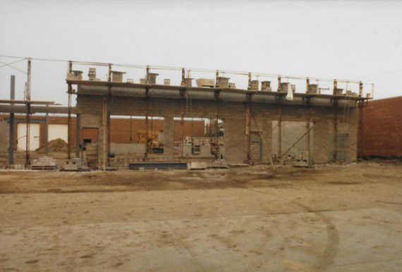 Construction site with exposed concrete structure, scaffolding, and surrounding brick buildings under construction.