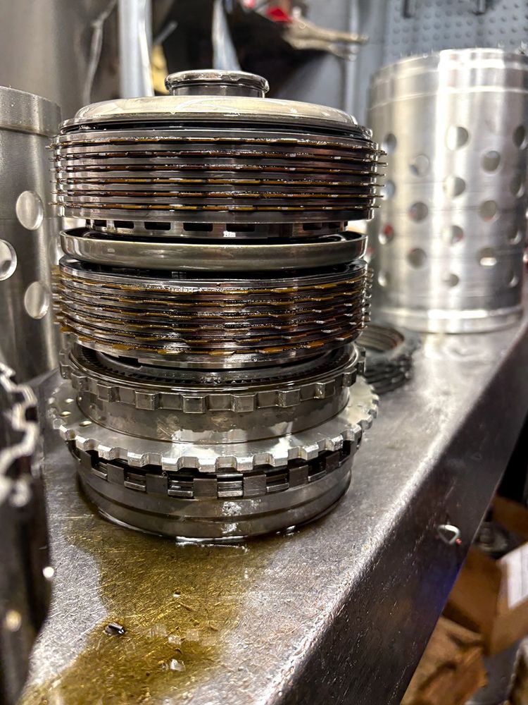 Stacked transmission clutch plates on a workbench. Wet, with metal housing in the background.