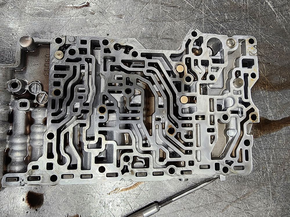 Transmission valve body with intricate channels, viewed from above, on a metal surface.