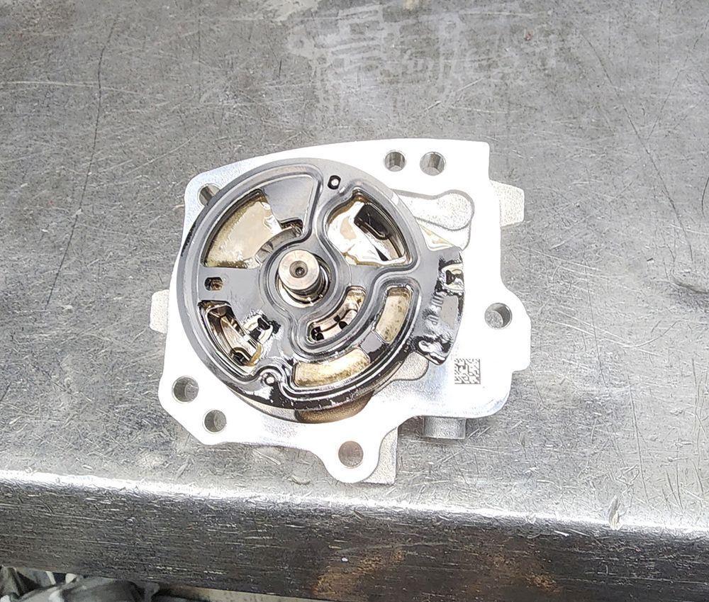 Oil pump, disassembled, lying on a metallic surface, showing internal components covered in oil.