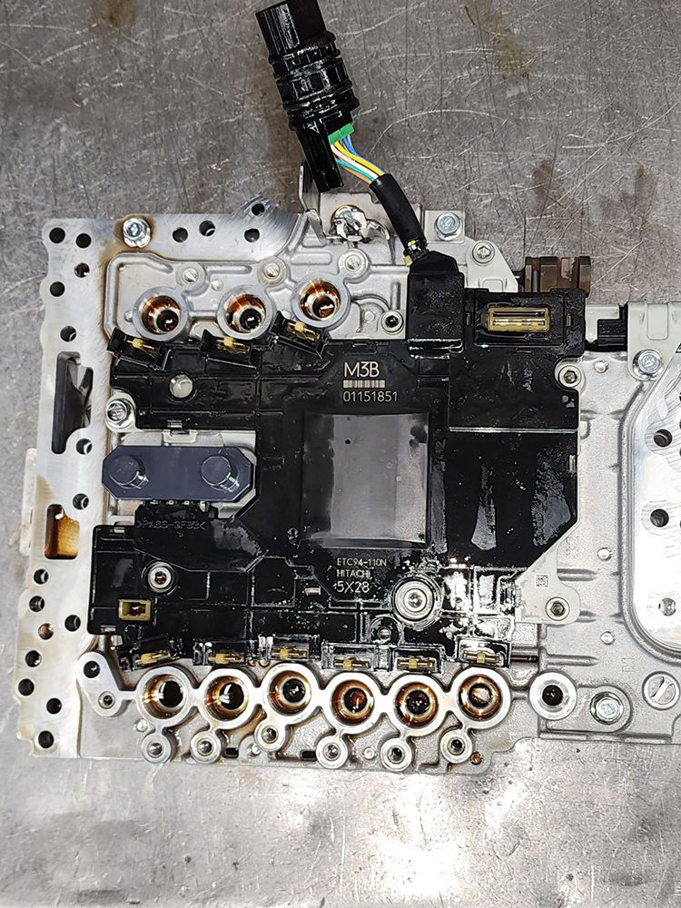 Transmission valve body with solenoids and electrical connector, on a metal surface.